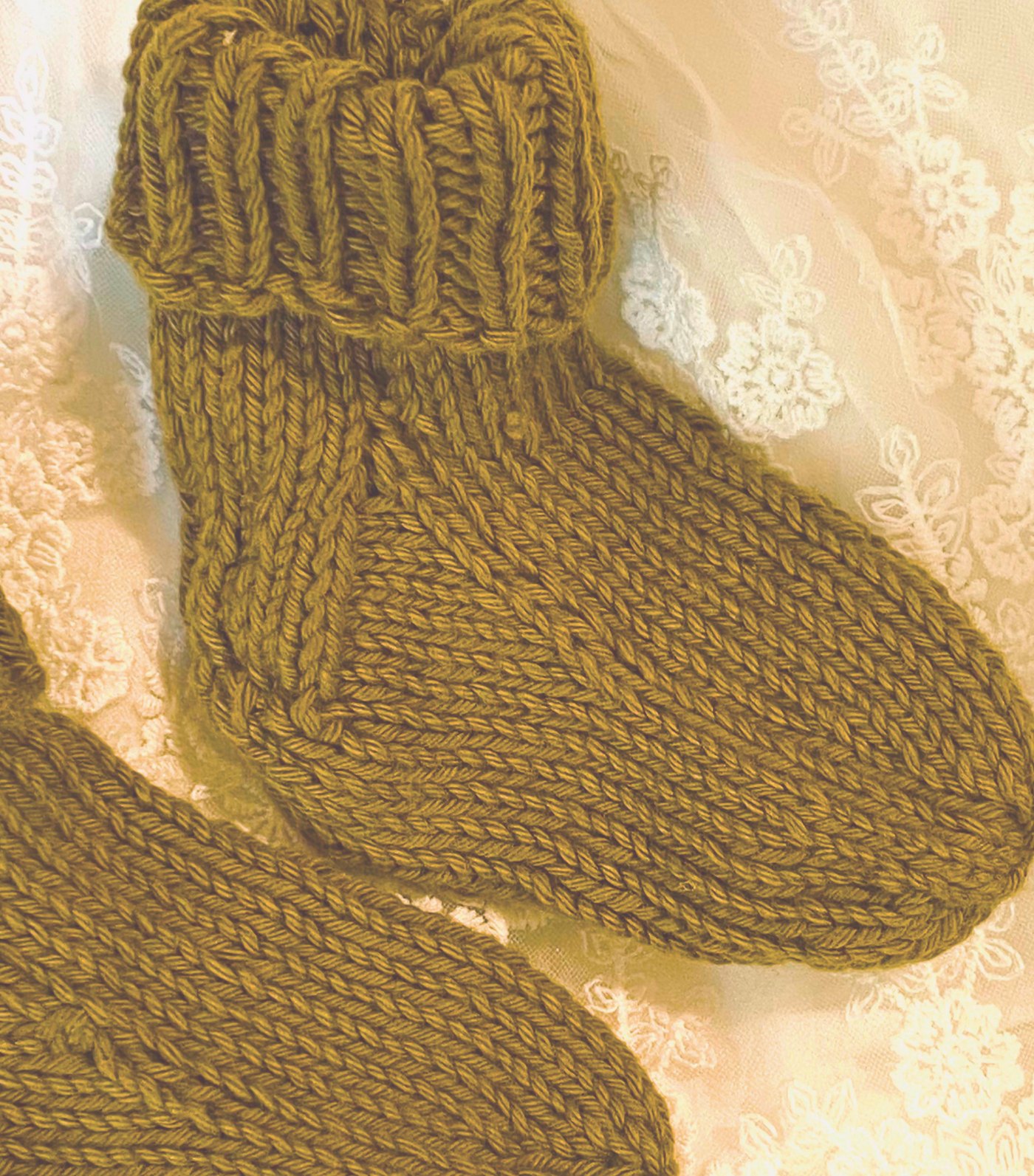 A pair of olive knitted booties resting on lace