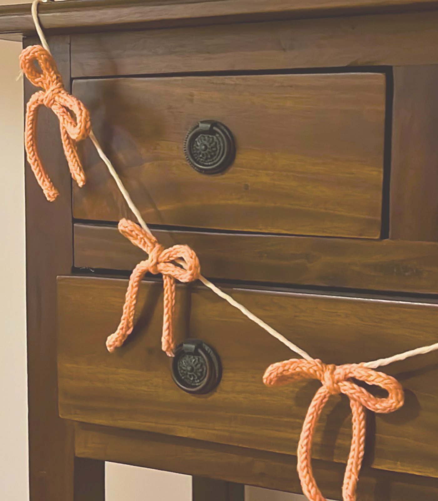 A garland of small orange knitted bows strung across a wooden dresser