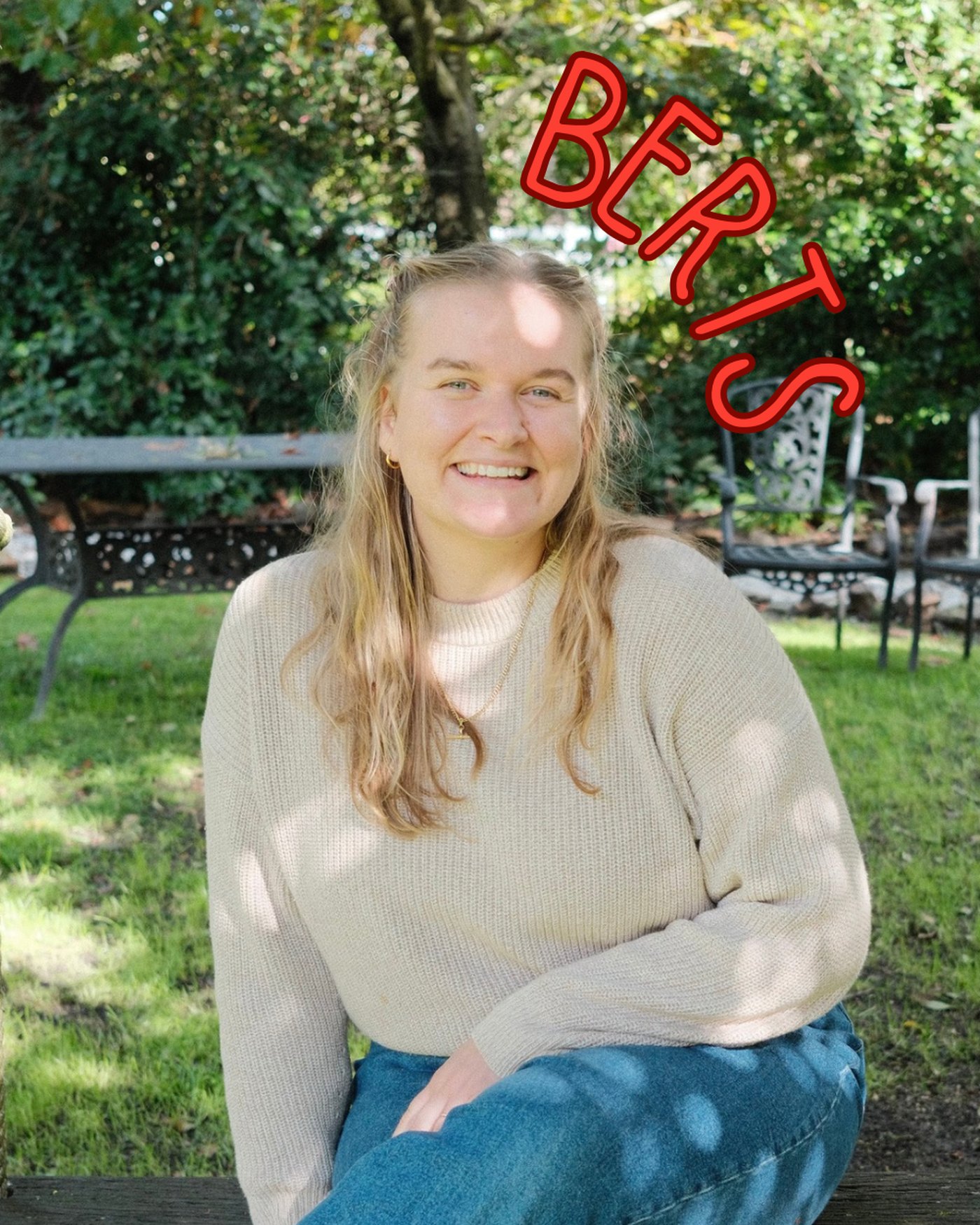 Lydia sitting on a swing in a garden, laughing, in a cream knit jumper.