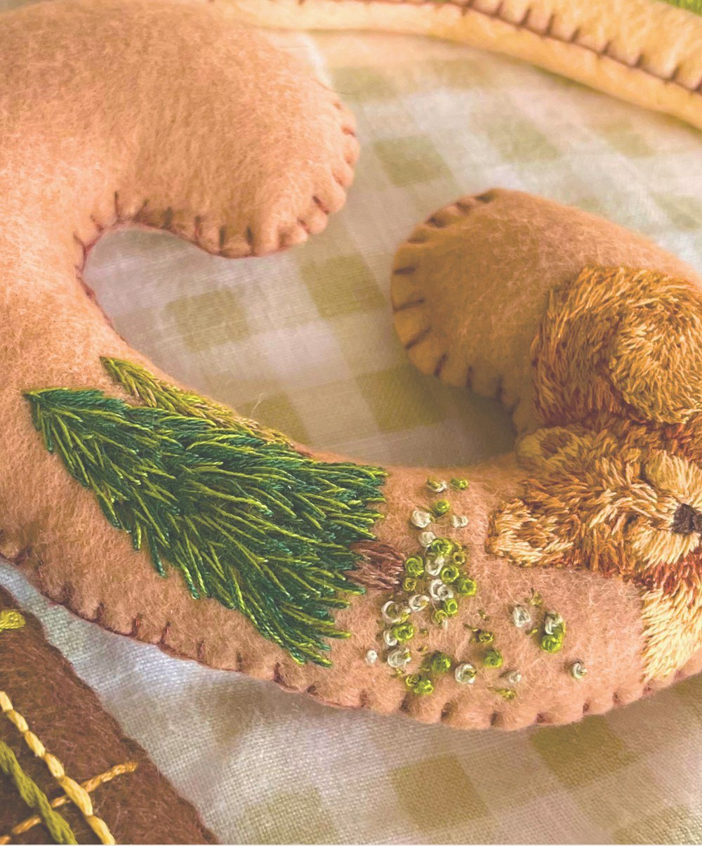 A felt letter embroidered with a sleeping squirrel and a pine tree