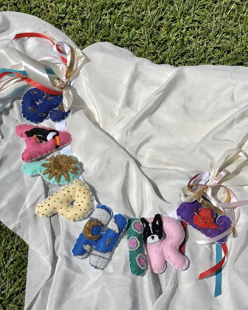 A long beaded felt letter banner laid out on white silk on the grass
