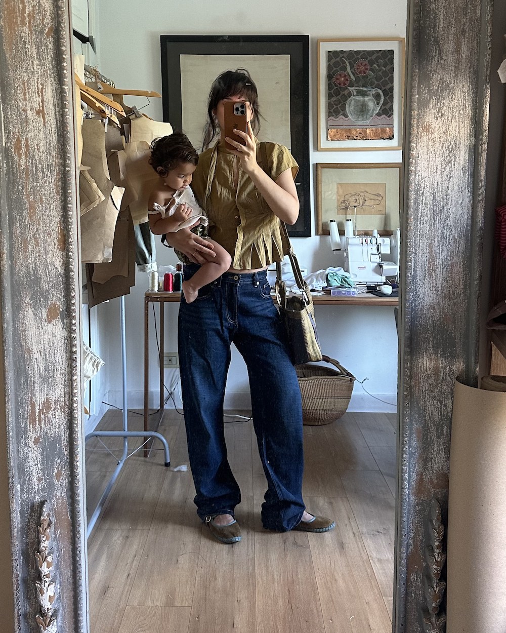 Joaquina holding Sira in front of a tall mirror in her studio, pattern pieces on a rail behind them