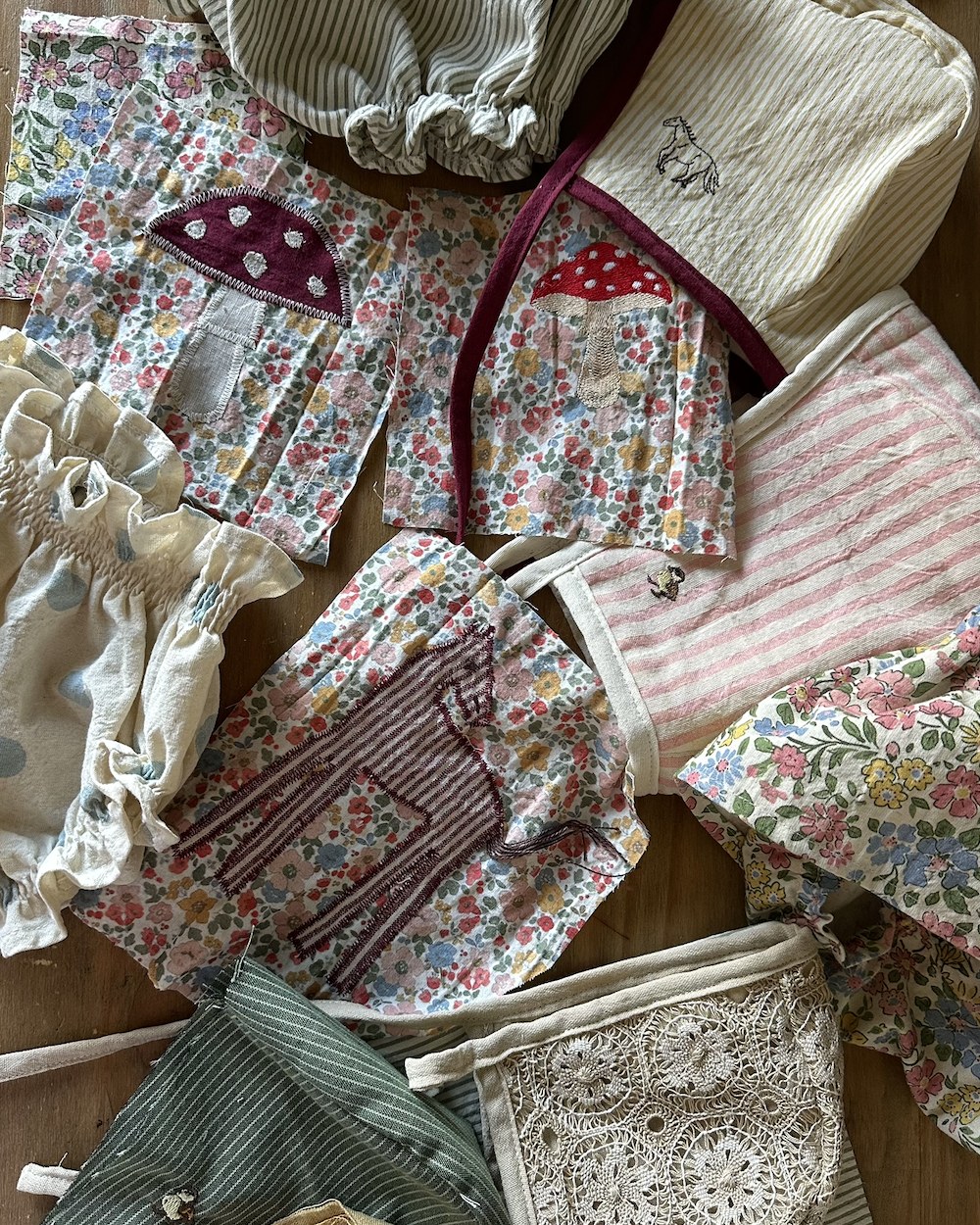 Pieces in progress laid across a wooden table, toadstools and animals embroidered onto floral cotton
