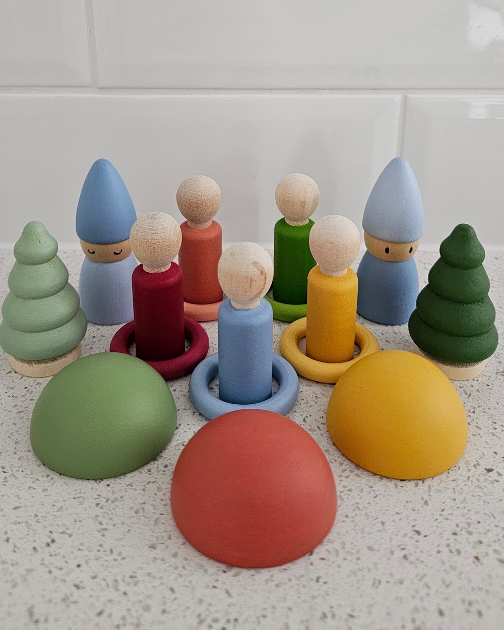 A group of painted wooden gnomes, peg dolls and little trees on a kitchen bench