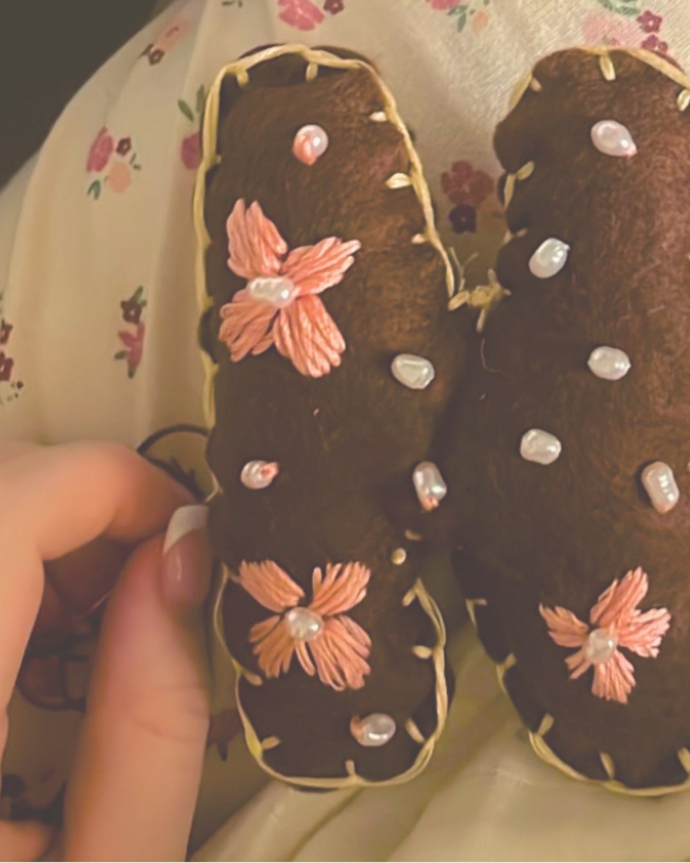 A brown felt letter beaded with pearls and coral flowers, held in one hand