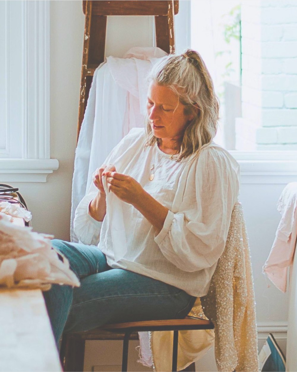 Aimee sewing by the window in her studio