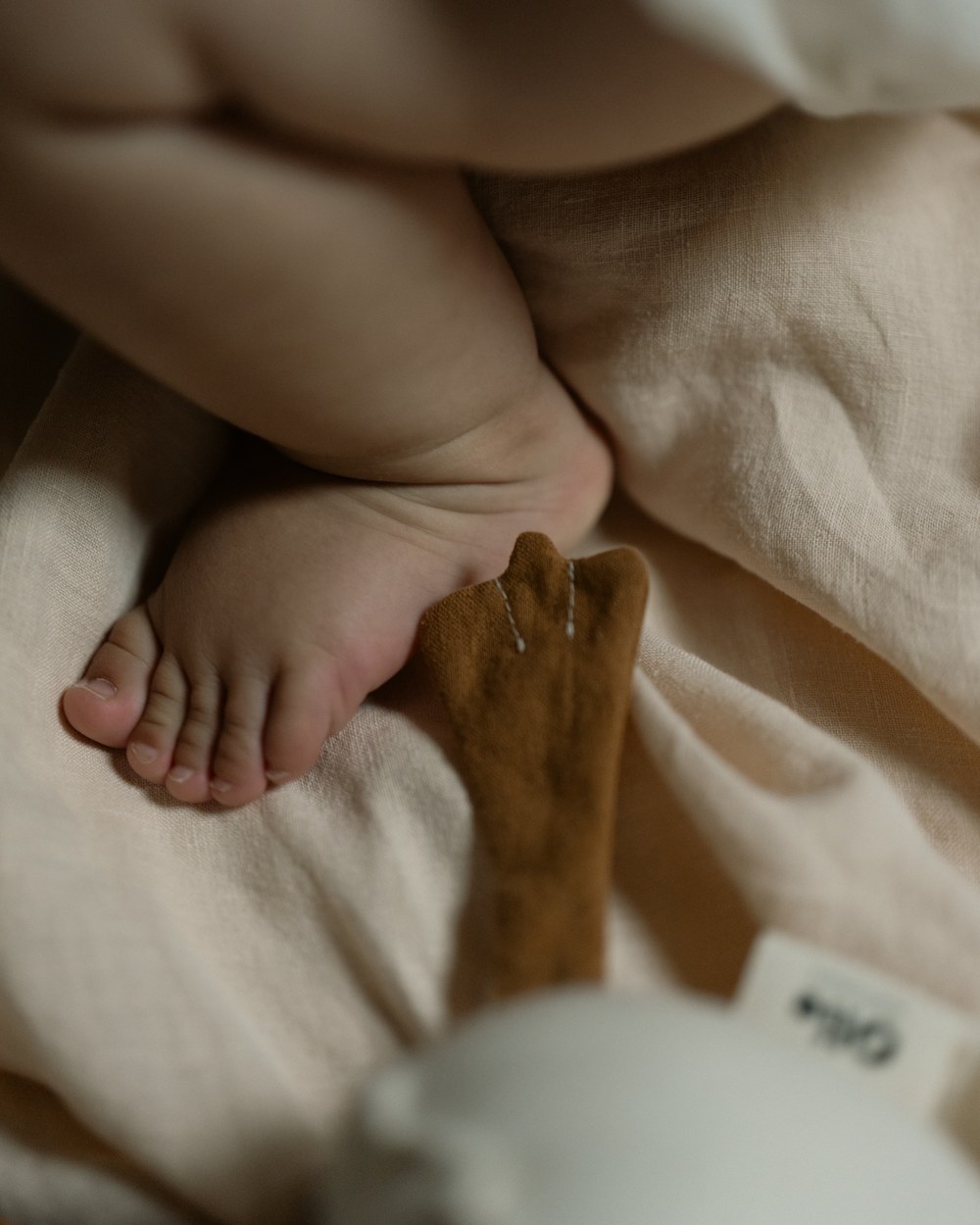 A baby's foot beside the goose's mustard felt feet on a linen sheet