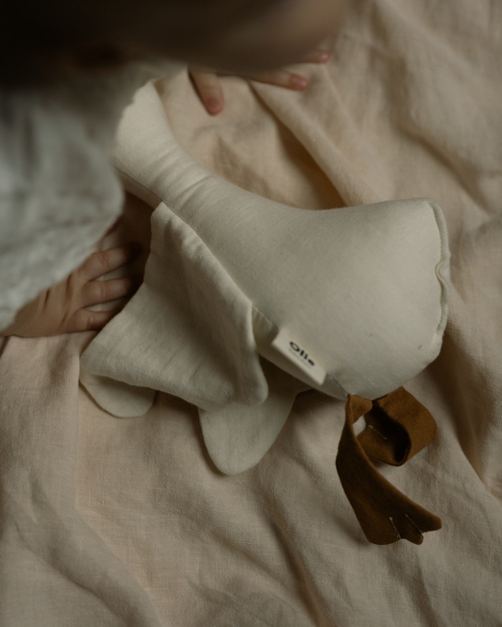 A baby lying on linen with the Cozy Goosey tucked in beside them