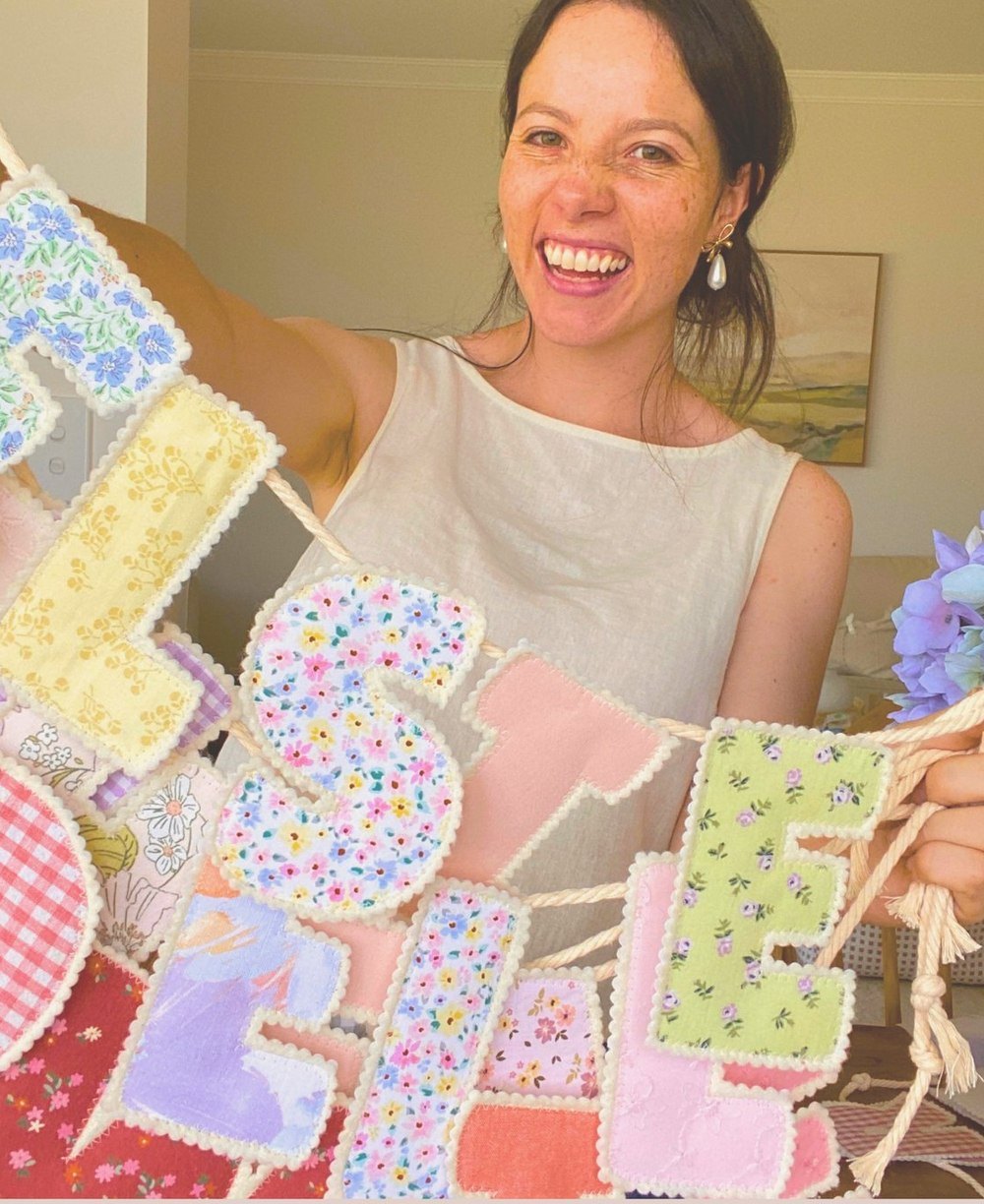 EJ smiling, holding up a large floral bunting