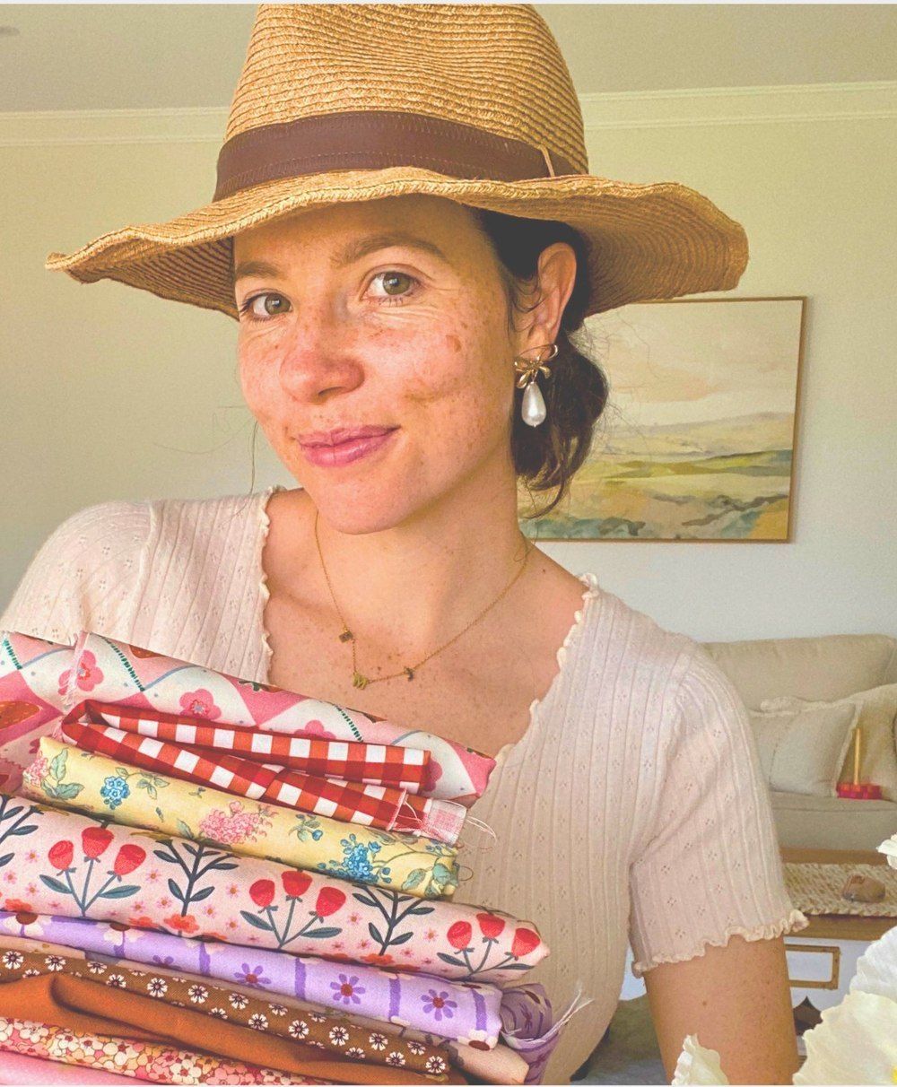 EJ in a straw hat, holding a stack of folded floral fabrics
