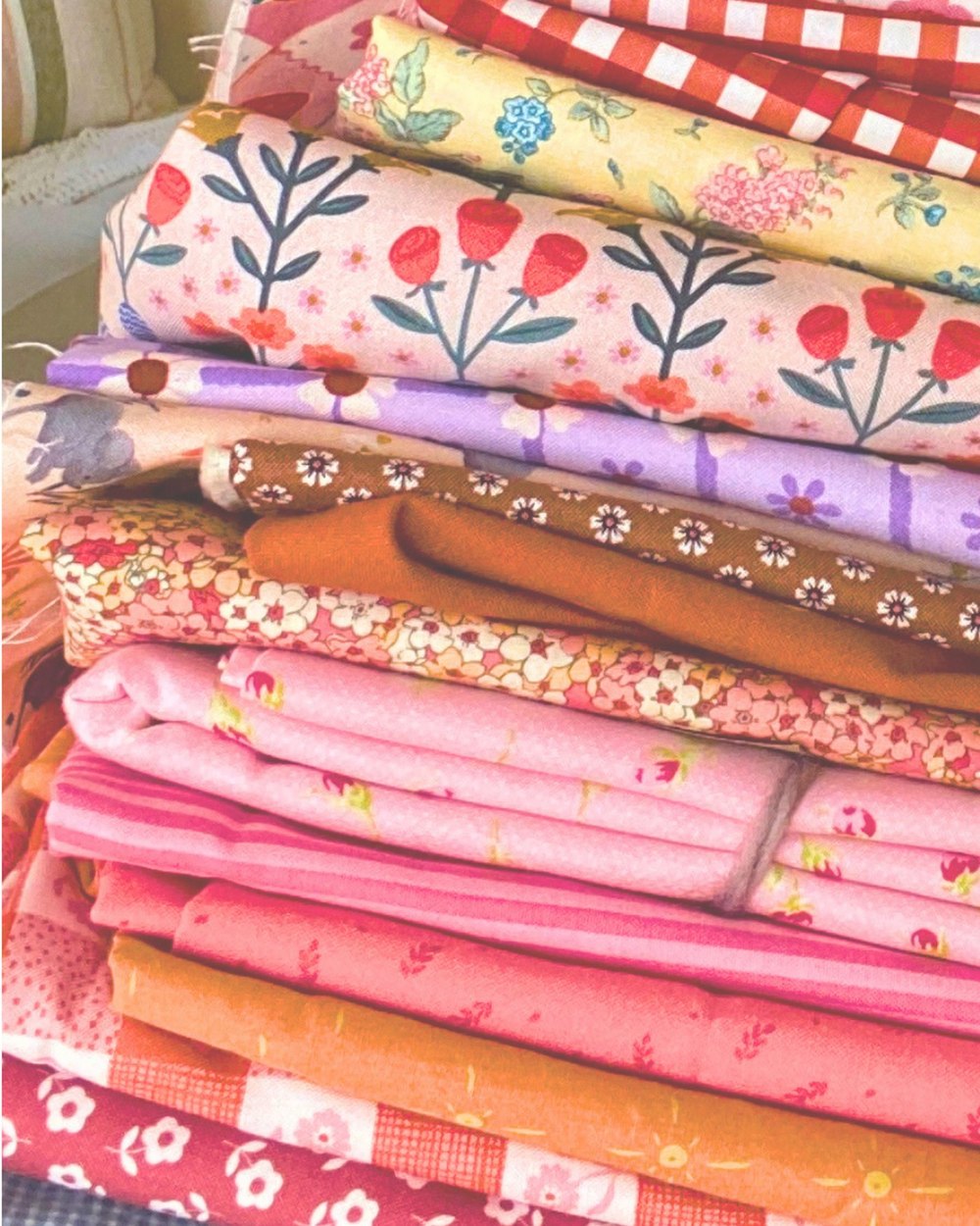 A tall stack of folded floral and gingham fabrics