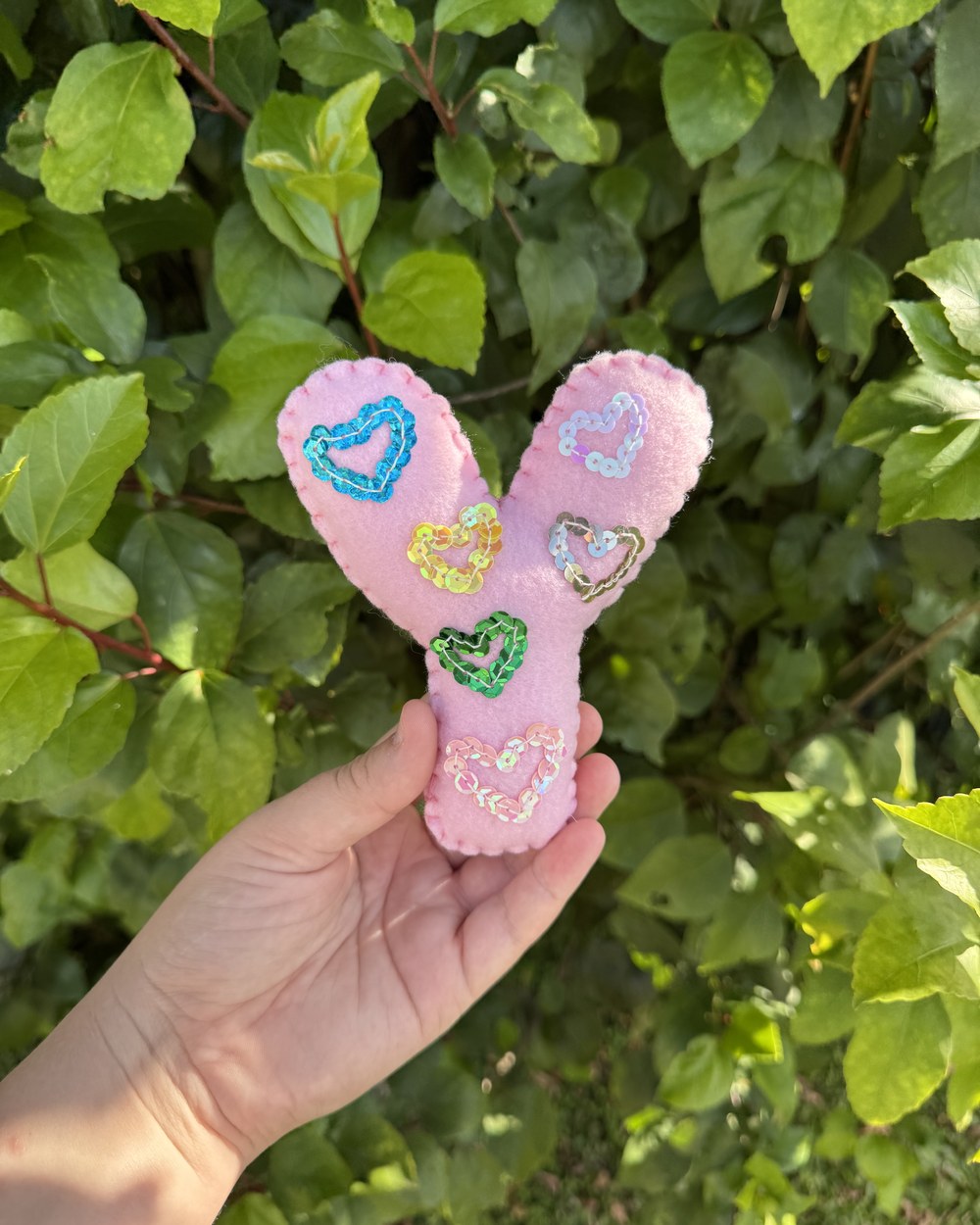 A pink felt letter held in one hand, stitched with sequin hearts