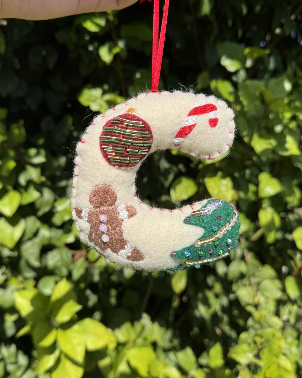 A felt letter ornament on a red ribbon, embroidered with a gingerbread man, a candy cane and a Christmas tree